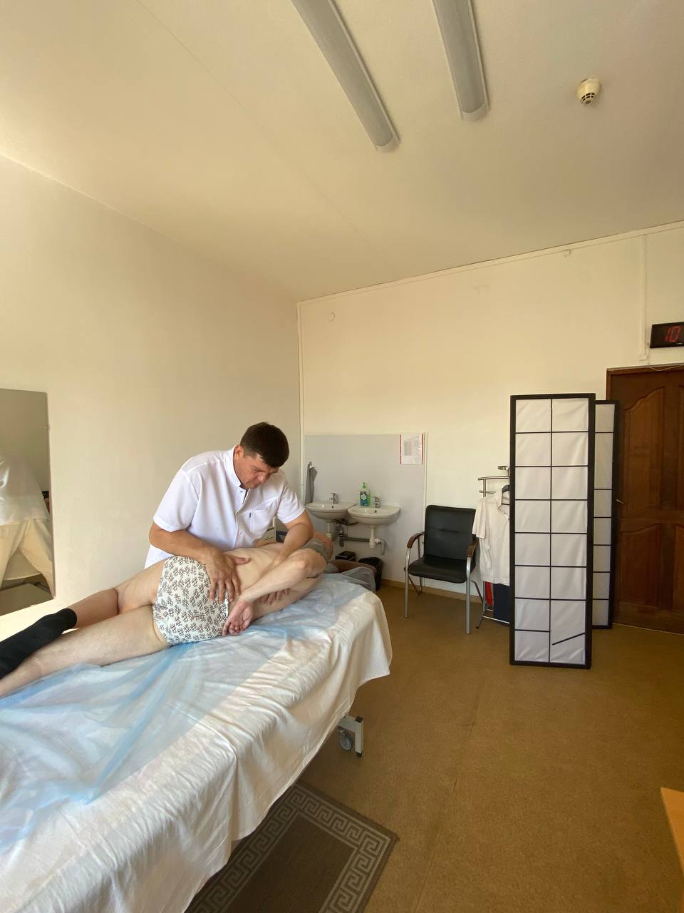 ассажист работает с пациентом на массажном столе, проводя мануальную терапию на области нижней части спины.